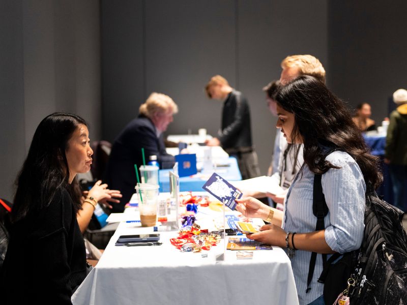 Photo of two people are talking over a booth looking over professional materials.