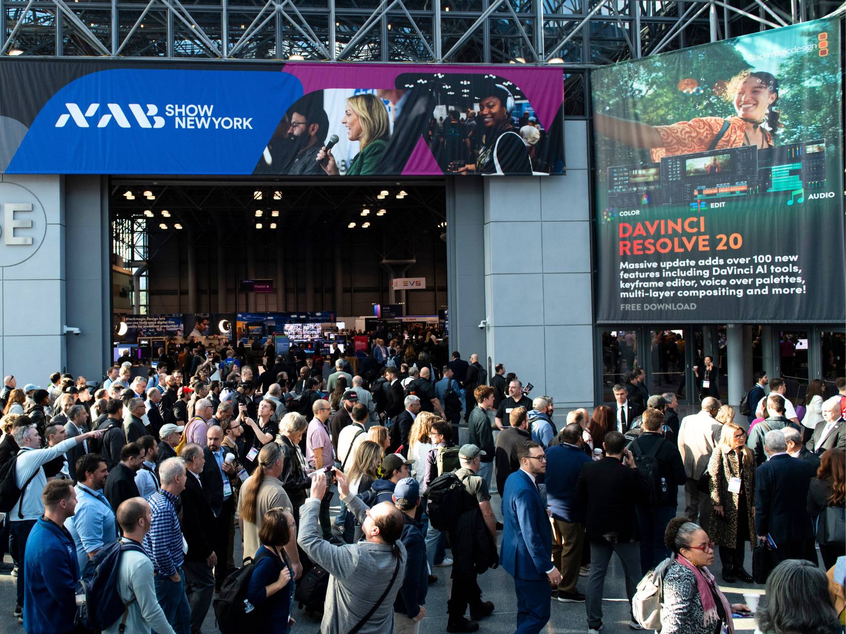 A crowd gathers below an entryway, filling a lobby, inside the Javitas Center for the 2025 NAB Show New York.